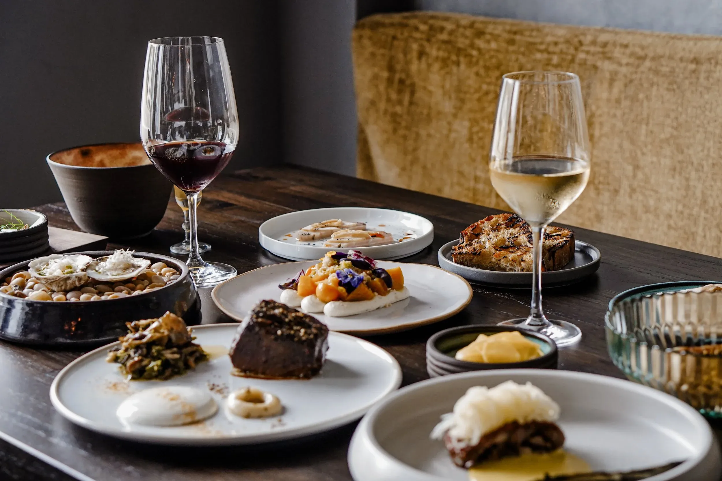 A spread of small plates with a glass of red and a glass of white wine on a wooden table